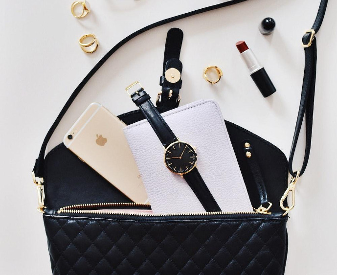 a black and white purse with a cell phone and a watch.